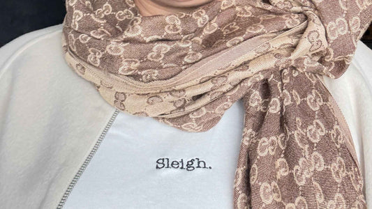 Close-up of the white Sleigh. organic cotton Christmas t-shirt layered under a cream jacket with a beige patterned scarf