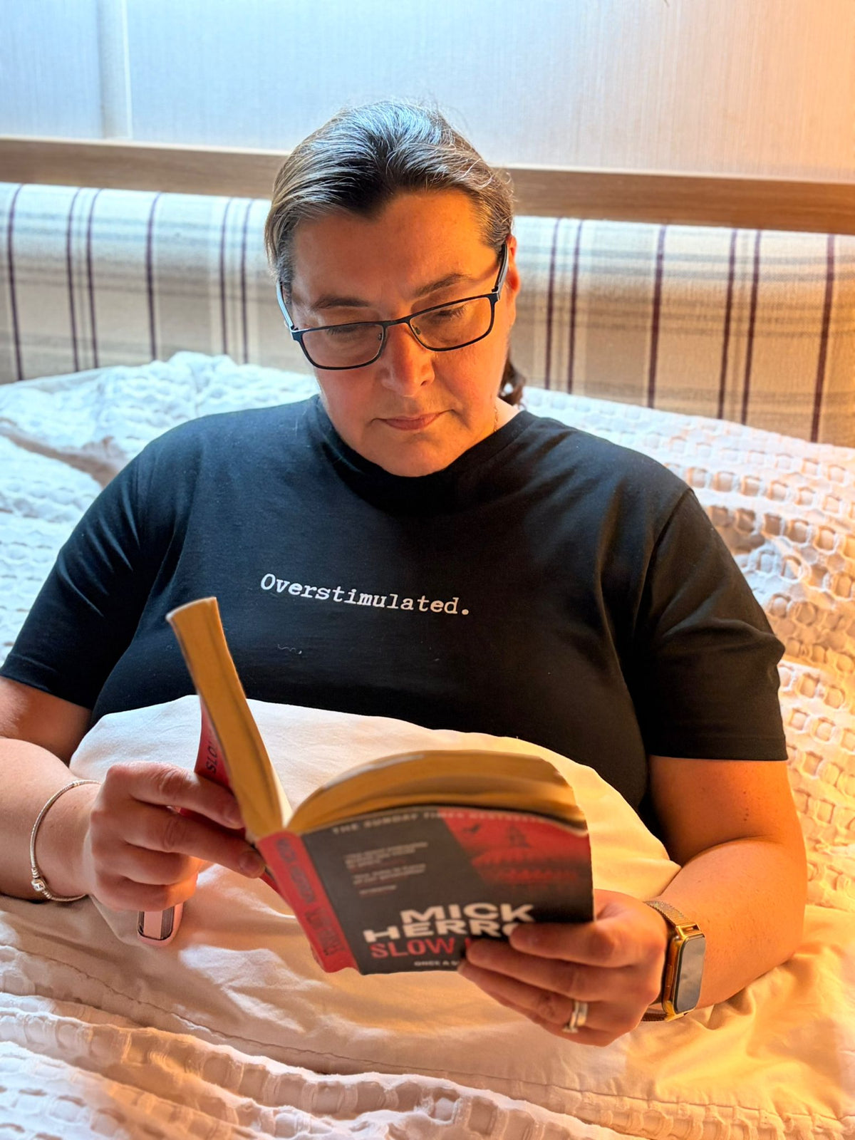 Woman wearing a pink t-shirt with 'Overstimulated' text against a brick wall.