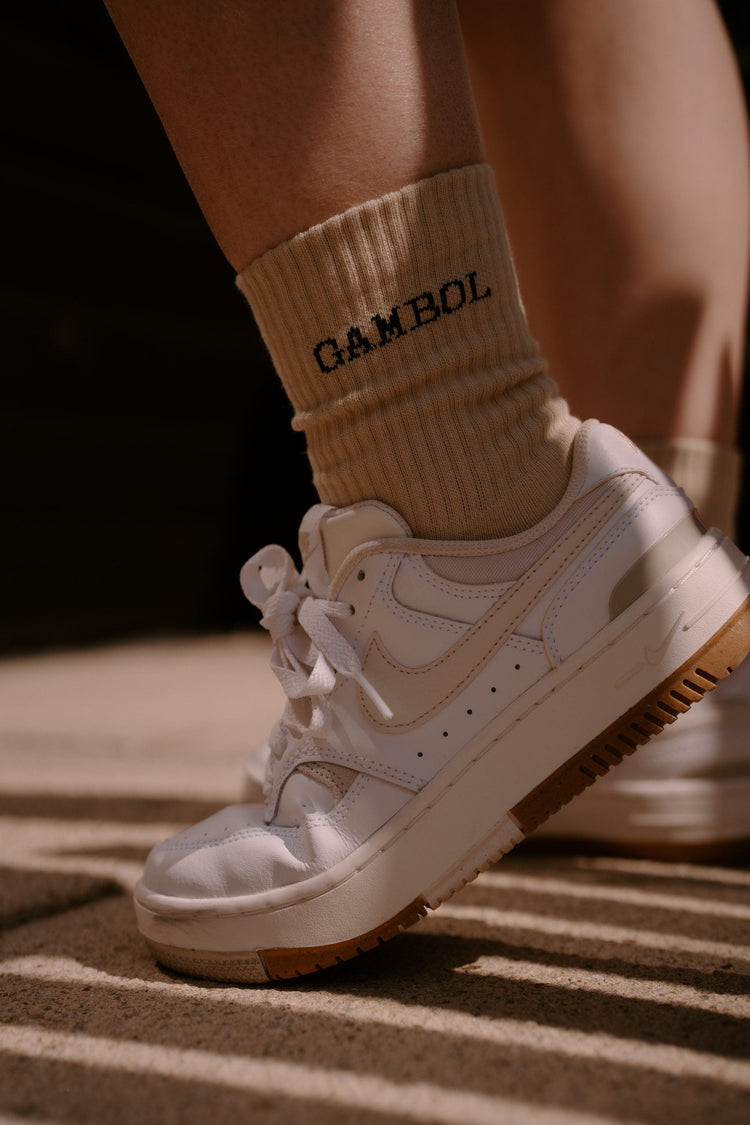 White sneakers with brown soles worn with beige socks featuring 'CAMEL' branding.