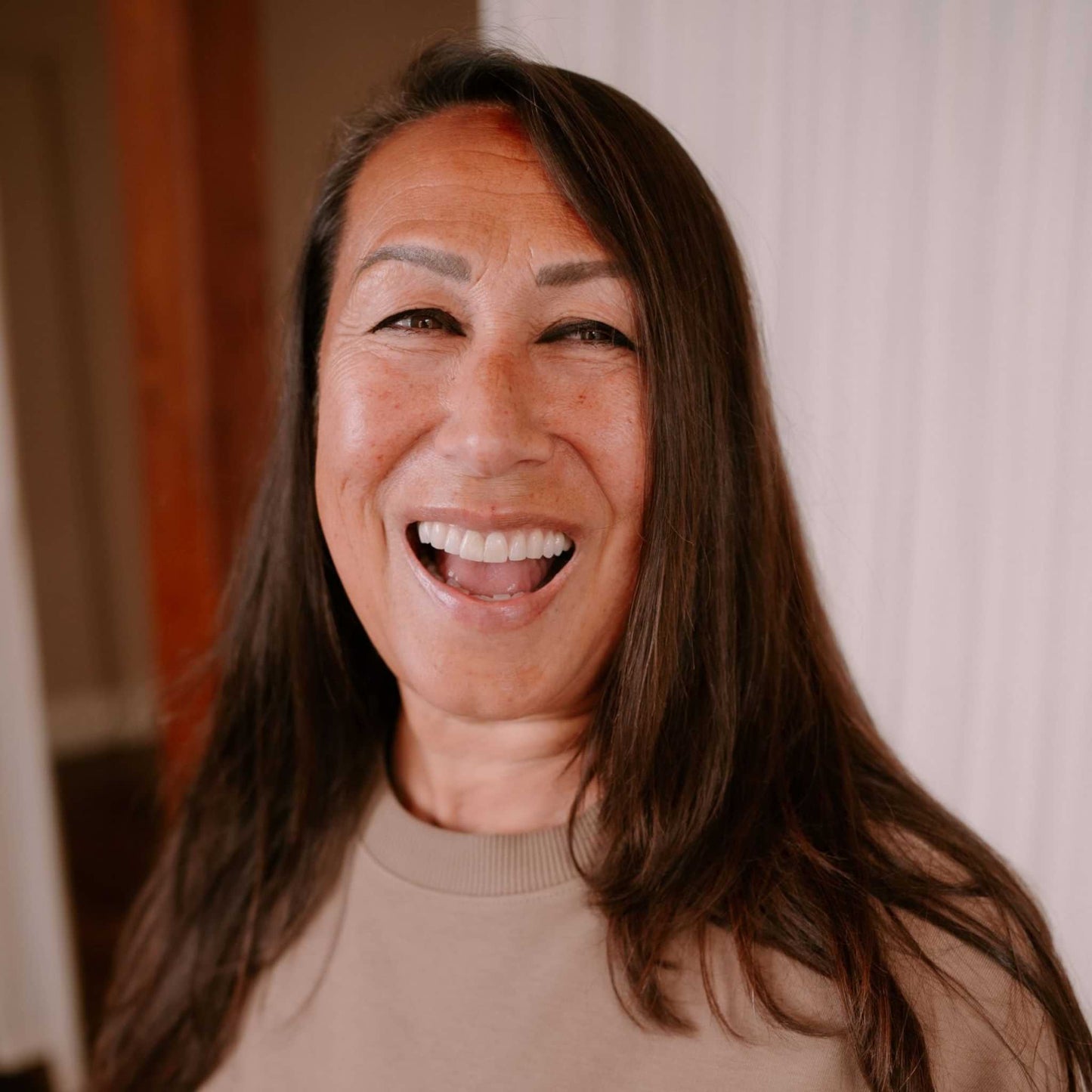 Woman with long brown hair smiling in front of a neutral background