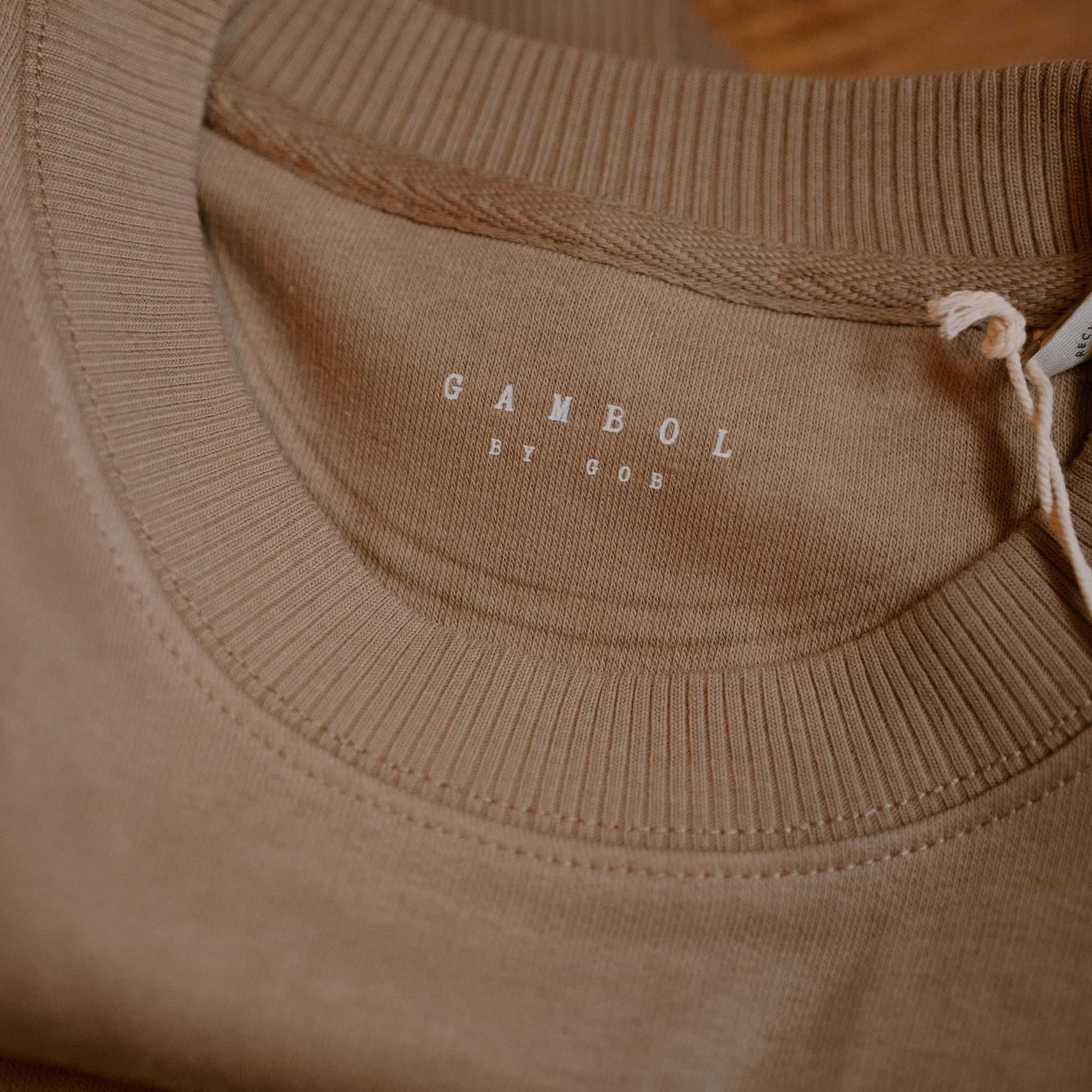 Close-up of a brown sweater with 'Gambol by Gob' branding on the collar.