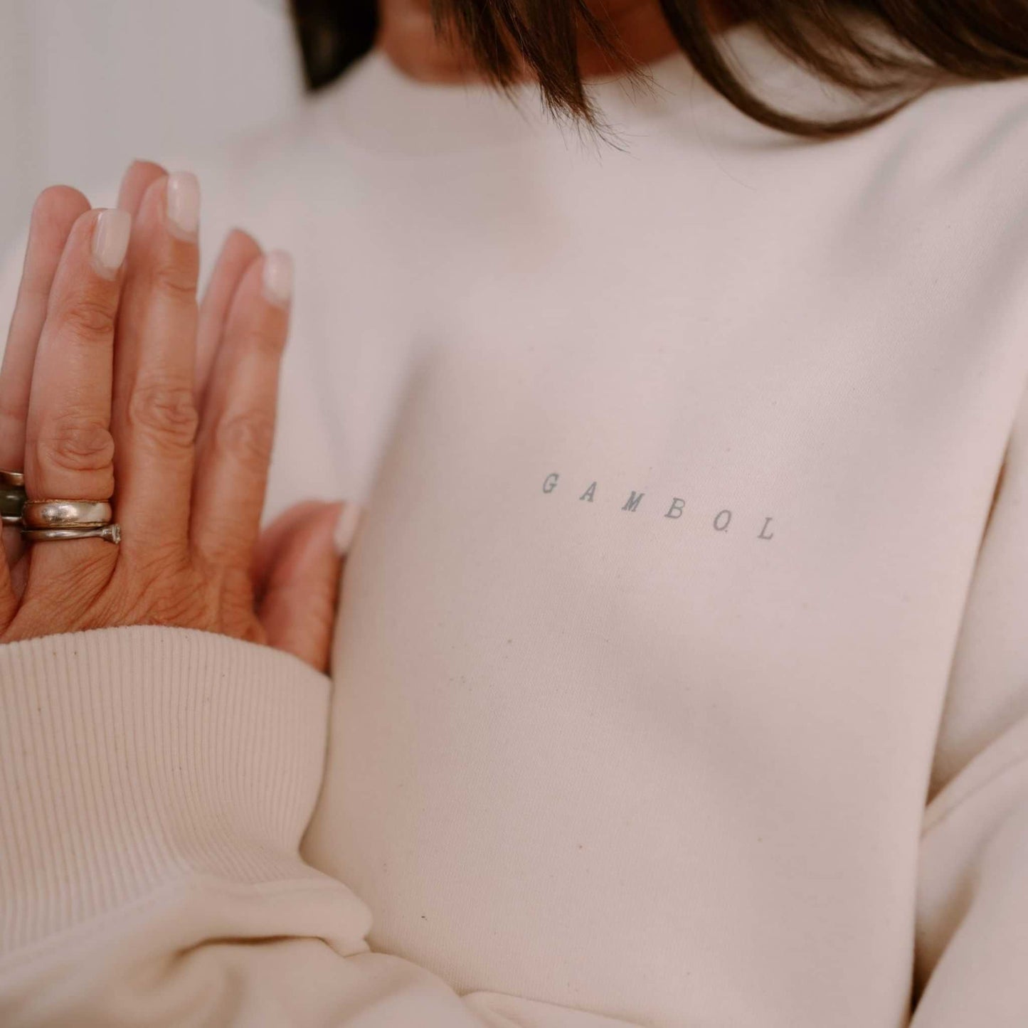Person wearing a beige sweater with 'GAMBOL' branding, holding hands together.