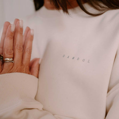 Person wearing a beige sweater with 'GAMBOL' branding, holding hands together.