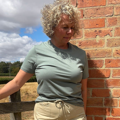 Blonde woman with curly hair wearing moss green complicated co t-shirt