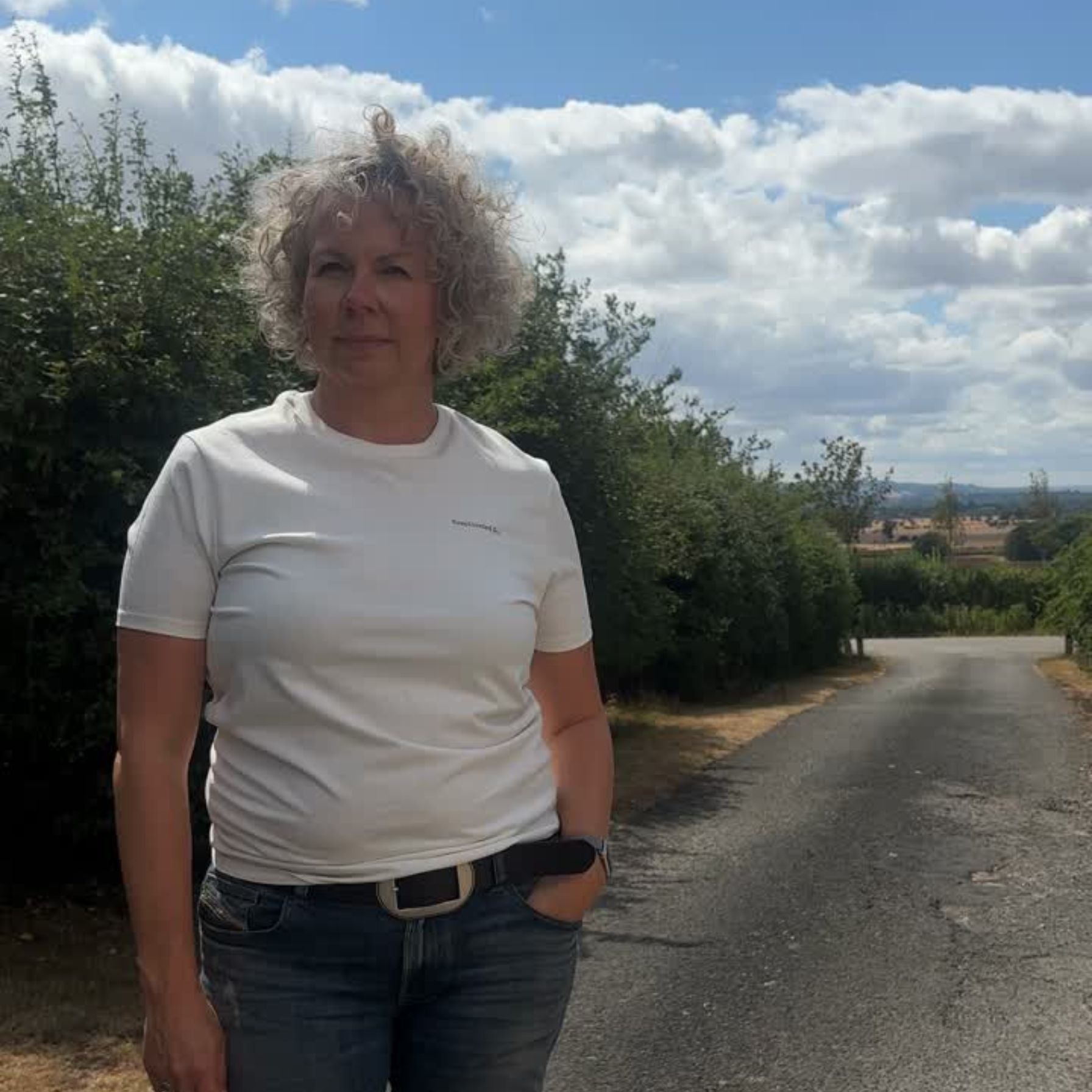 woman with blonde curly hair wearing white complicated co t-shirt and blue jeans