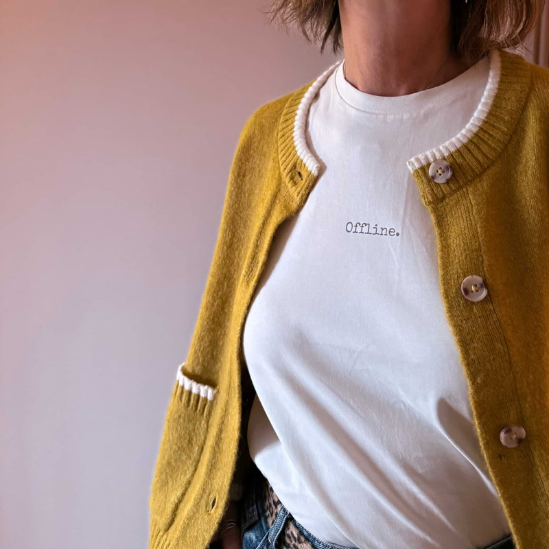Person wearing a mustard yellow cardigan over a white shirt with 'offline' text on a blurred background