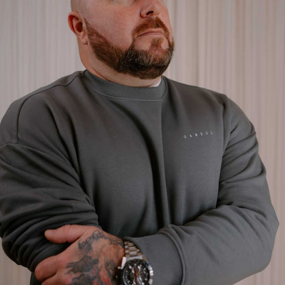 Man wearing a gray sweatshirt with a brand logo, standing against a neutral background.