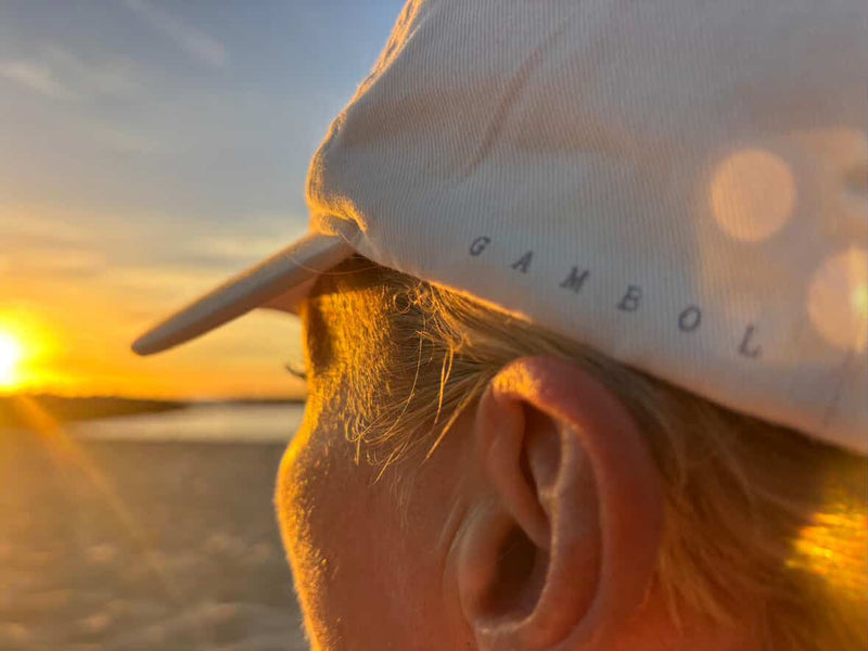 Person wearing a cap with 'Gambol' on it at sunset.