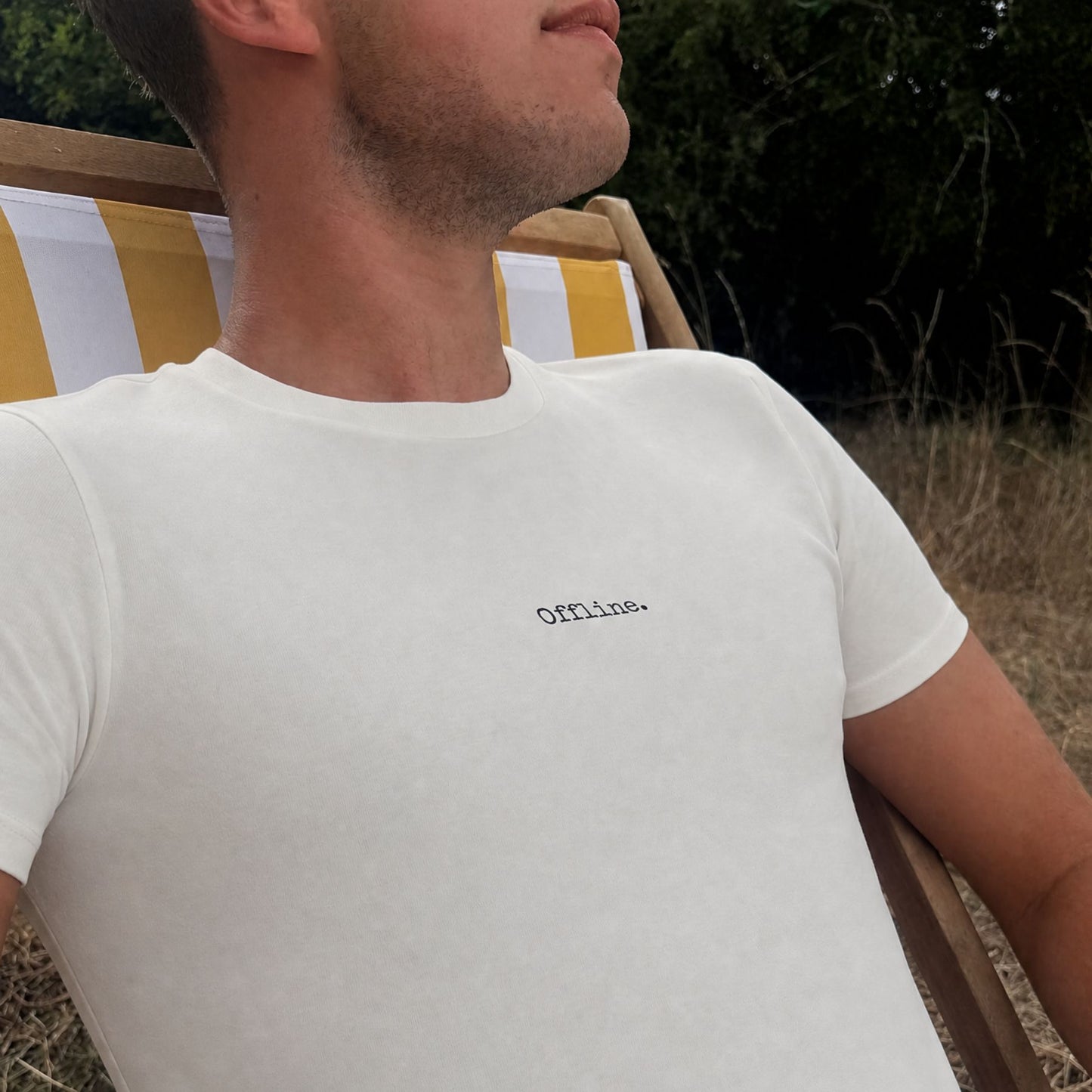 man sitting on a deck chair wearing an ivory t-shirt that says offline