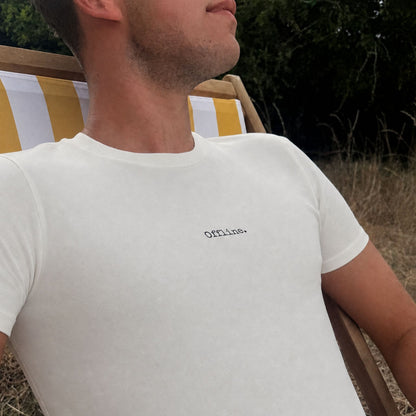 man sitting on a deck chair wearing an ivory t-shirt that says offline