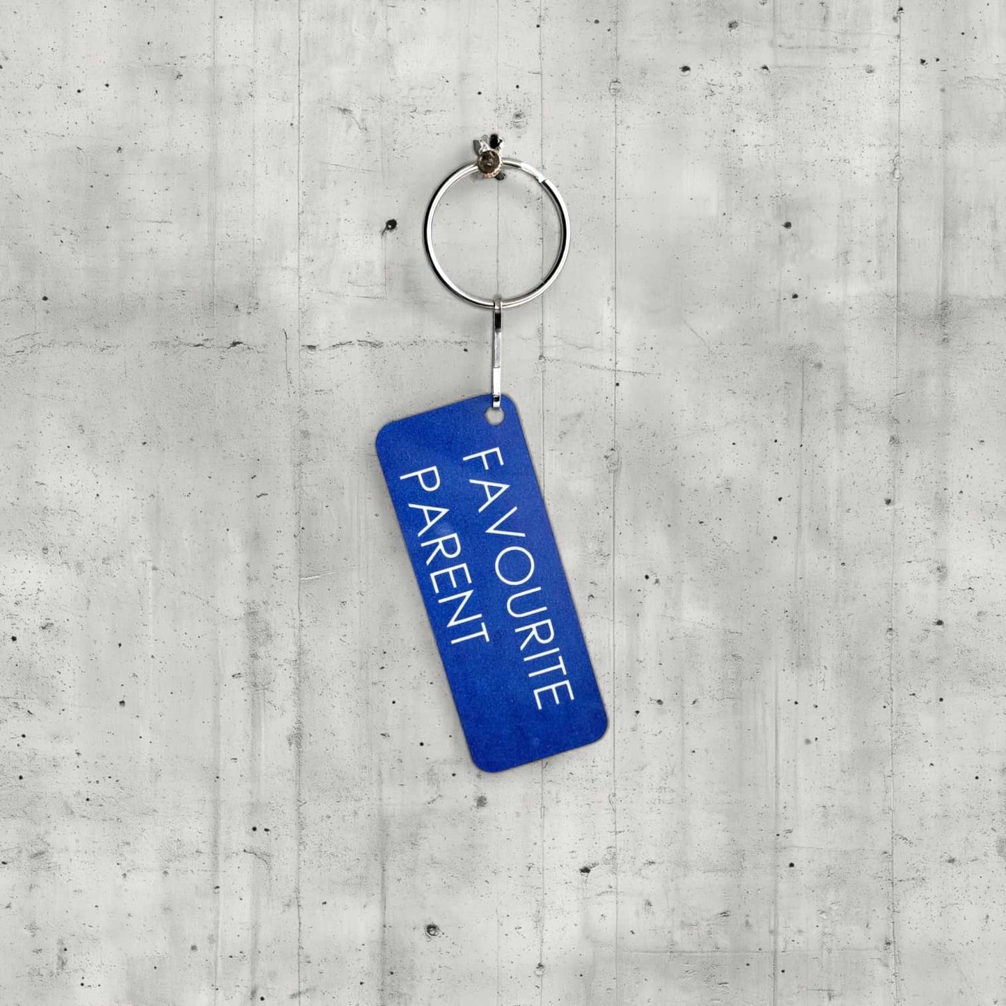 Blue keychain with 'FAVOURITE PARENT' text on a concrete surface