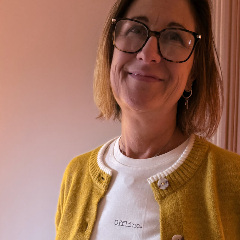 Woman wearing a yellow cardigan over a white shirt with text, standing against a plain background.