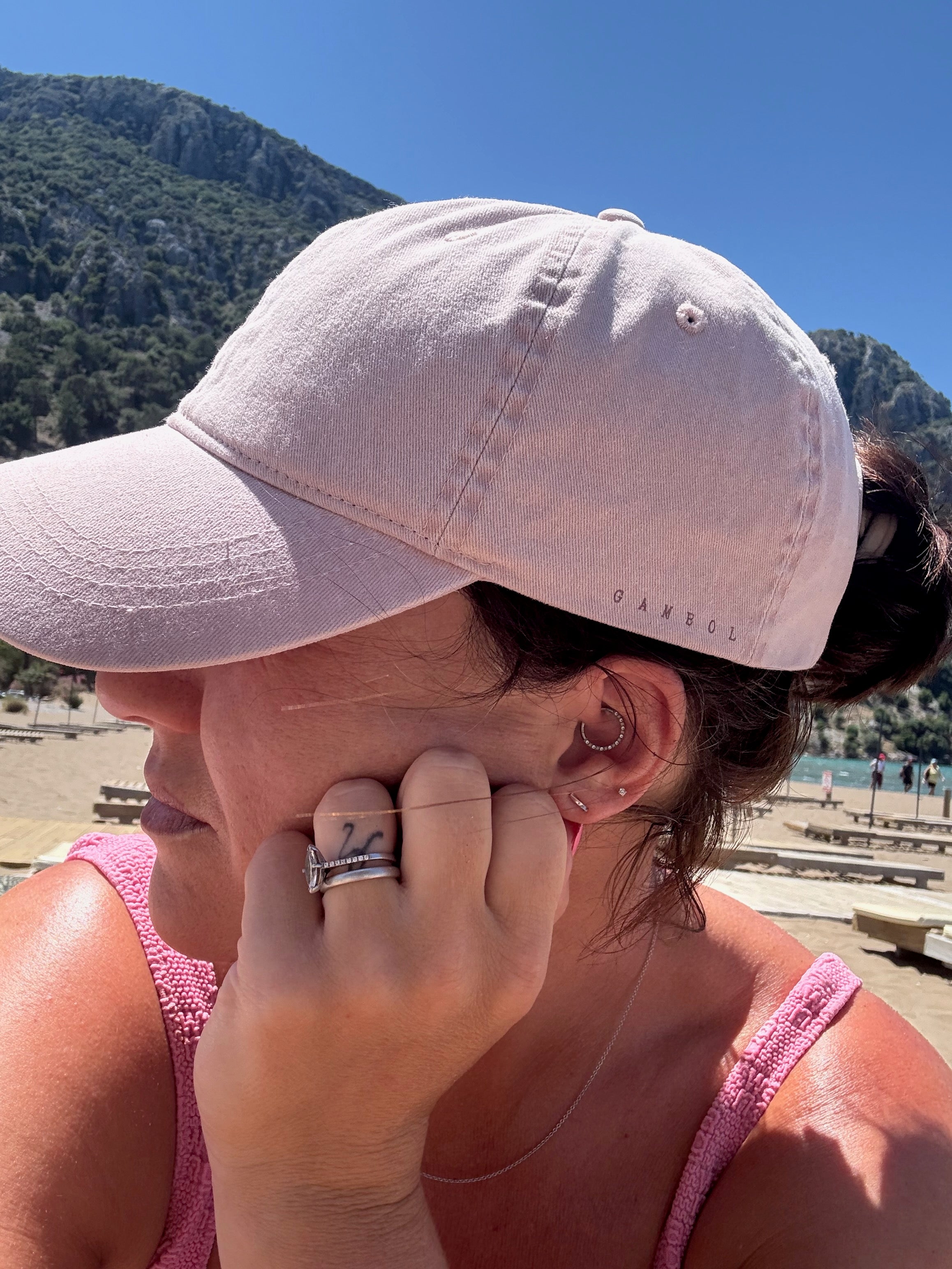 Woman wearing a pink cap on a beach with mountains in the background