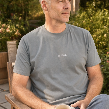 Man sitting outdoors holding a mug, wearing a gray t-shirt with text No Chat