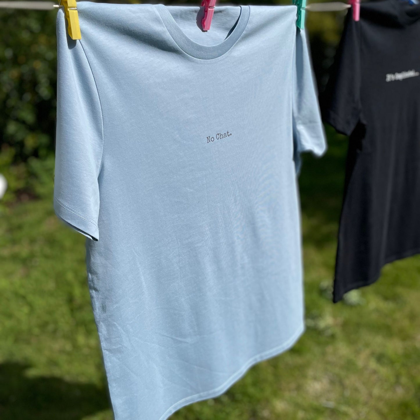 Light blue t-shirt with 'No Chat' text hanging on a clothesline outdoors.