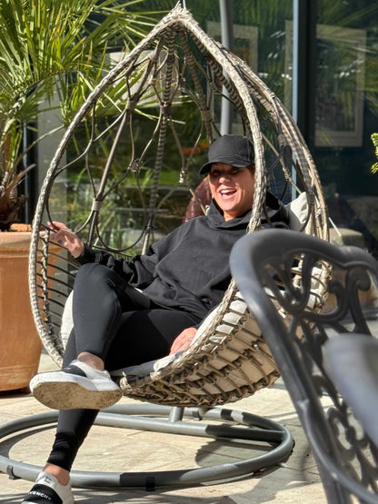 Person sitting in a hanging egg chair outdoors with plants in the background