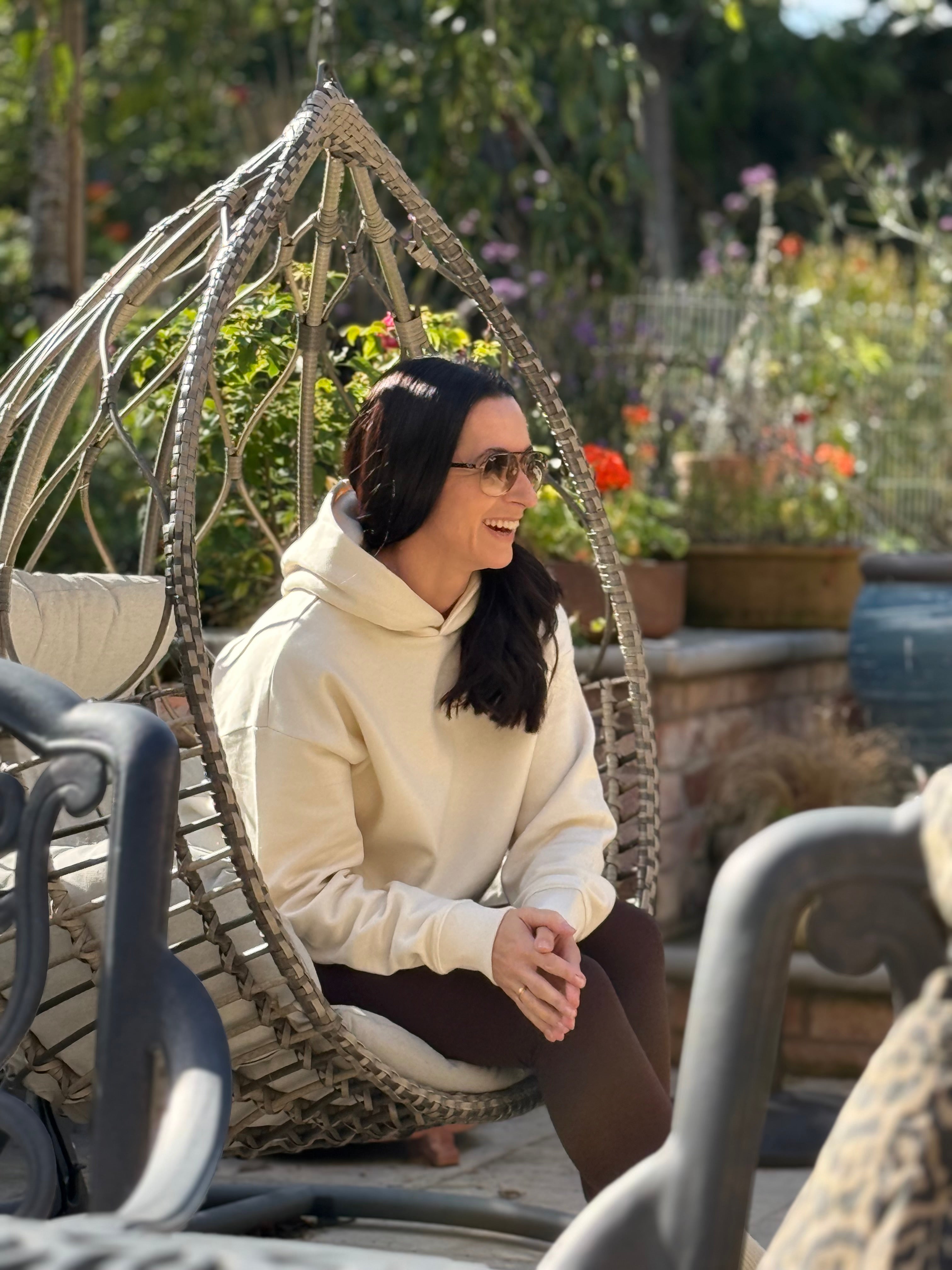 Woman in a cream hoodie sitting in a decorative chair in a garden setting