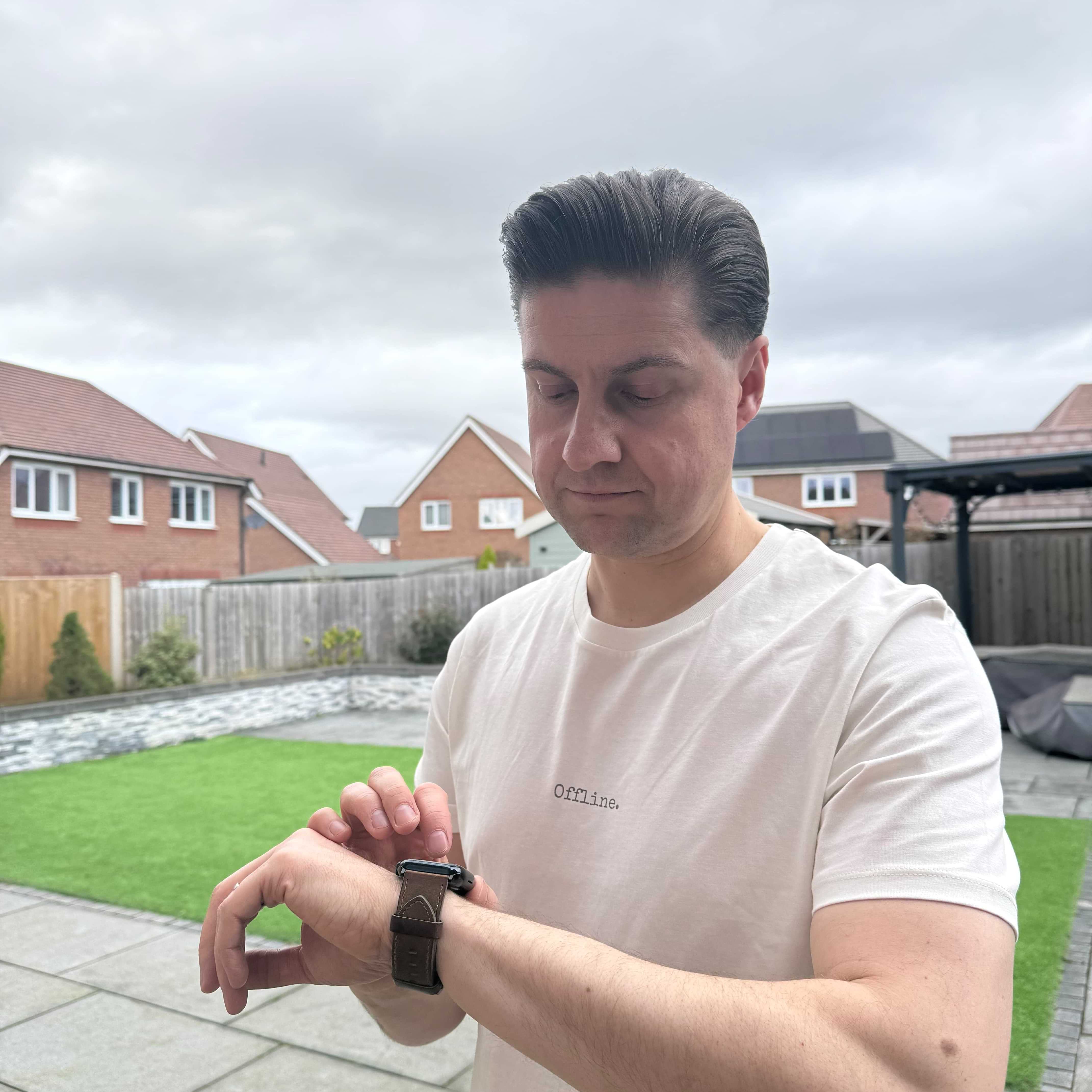 man with brown hair looking at his watch wearing offline white t-shirt