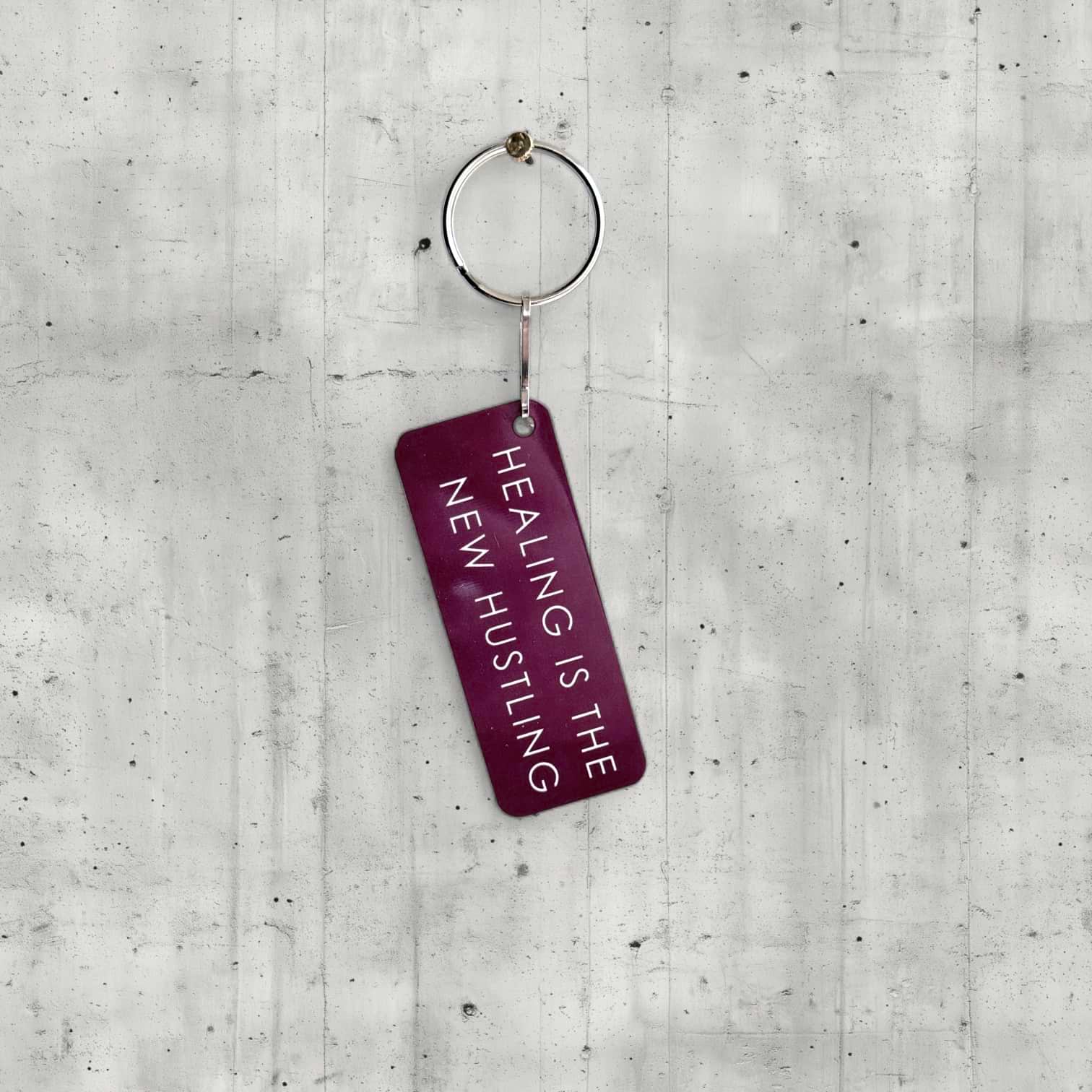 Keychain with 'Healing is the New Hustling' text on a concrete surface