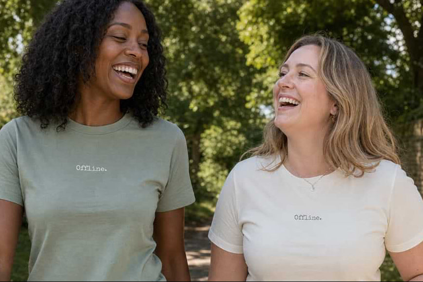 Two women walking outdoors wearing matching t-shirts and jeans.