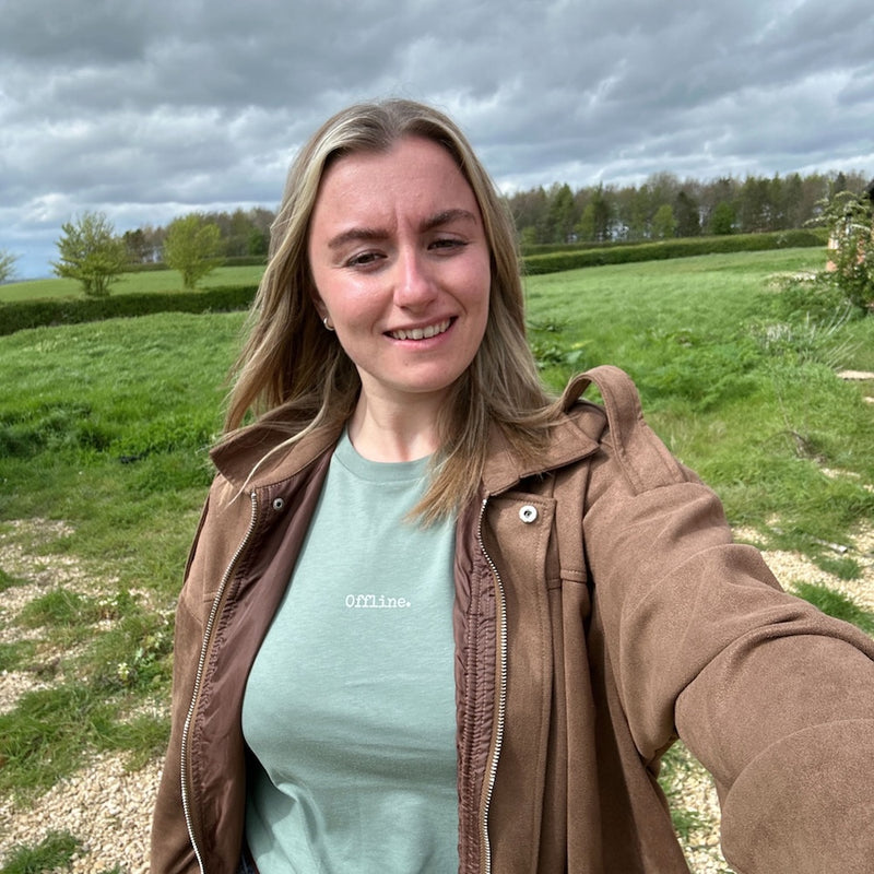 lady with blonde hair wearing green t-shirt with offline and brown jacket