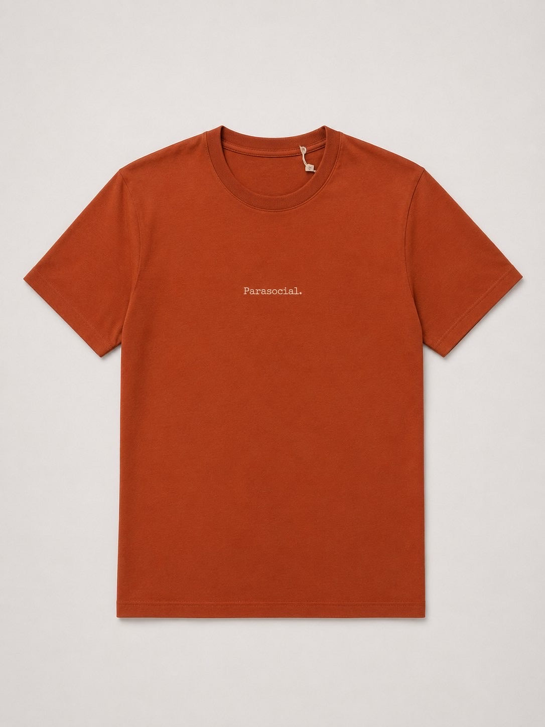A rust-orange crewneck t-shirt with the word 'Parasocial.' printed in small white text on the left chest, displayed flat against a light gray background.
