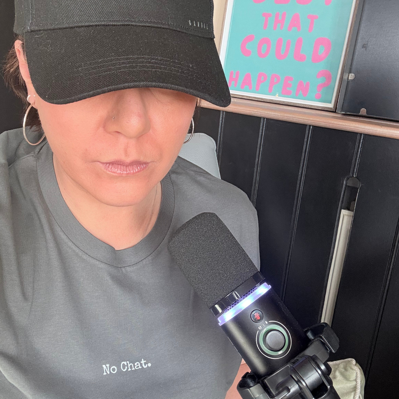 Person wearing a black cap and gray shirt with 'No Chat.' text, sitting in front of a microphone.