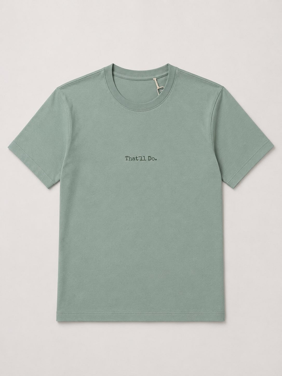 A sage green crewneck t-shirt with 'That'll Do.' printed in black text on the chest, displayed flat against a light gray background.