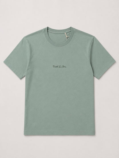A sage green crewneck t-shirt with 'That'll Do.' printed in black text on the chest, displayed flat against a light gray background.